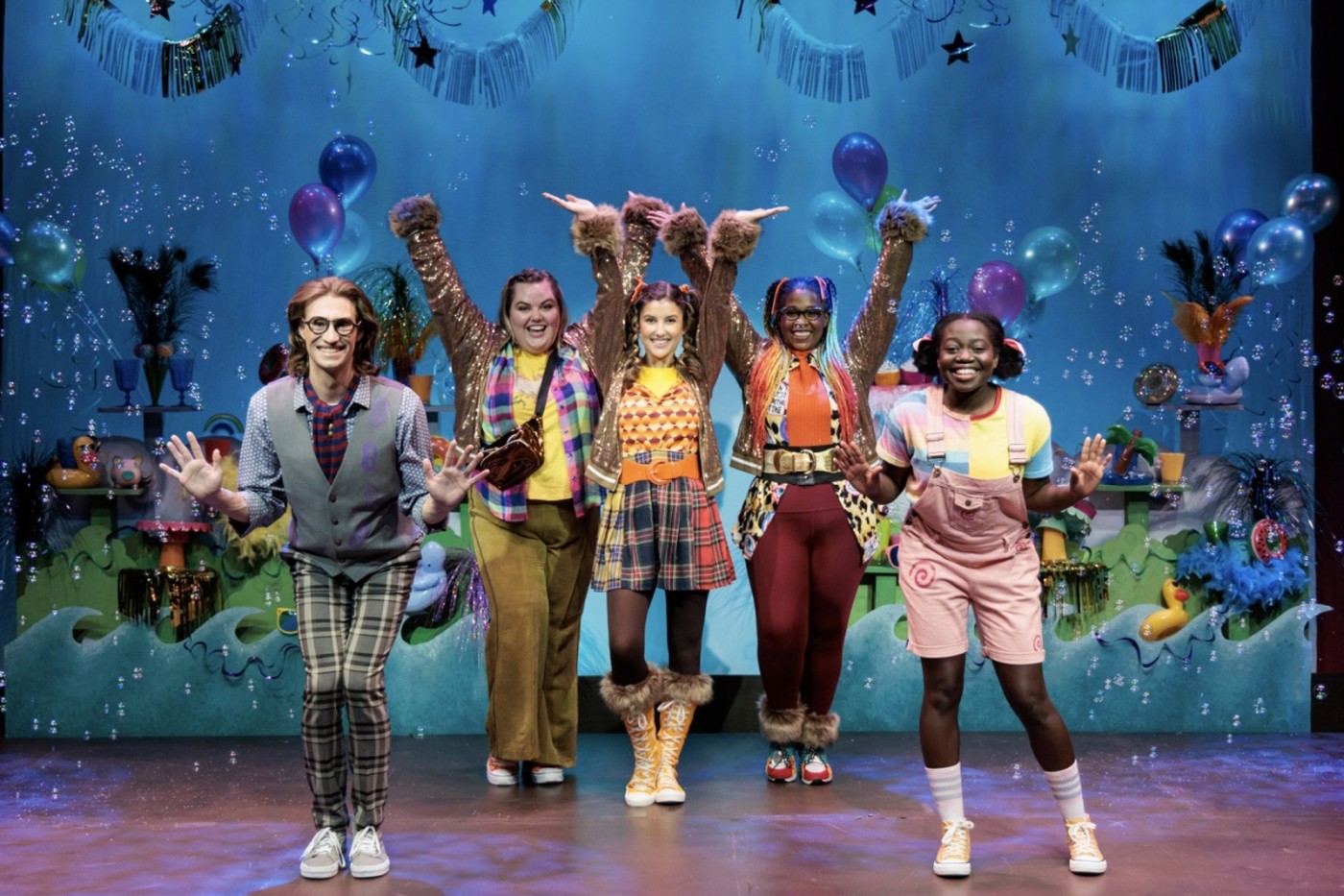 Five actors in eclectic outfits dancing with bubble on stage